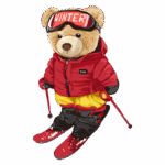 Urso de pelúcia vestido para esportes de inverno, usando jaqueta vermelha, calças amarelas e esquis vermelhos, com óculos de esqui e bastões. Ideal para ilustrações de temas de inverno e esportes na neve.